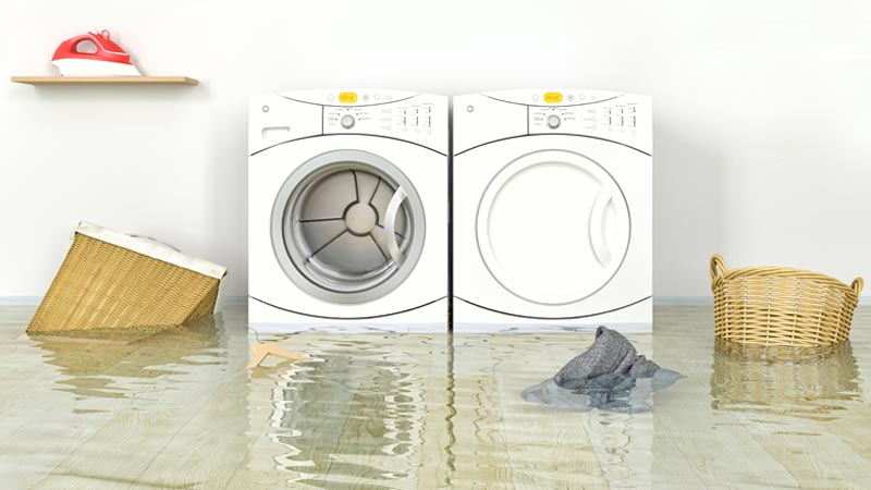 Duas máquias de lavar roupa, chão inundado de água, cestos a boiar, ferro de engomar na prateleira